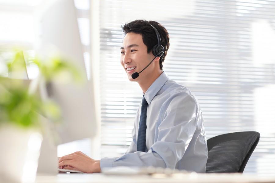 Atendente homem sorridente com headset usando computador, representando atendimento humanizado em marketplace.