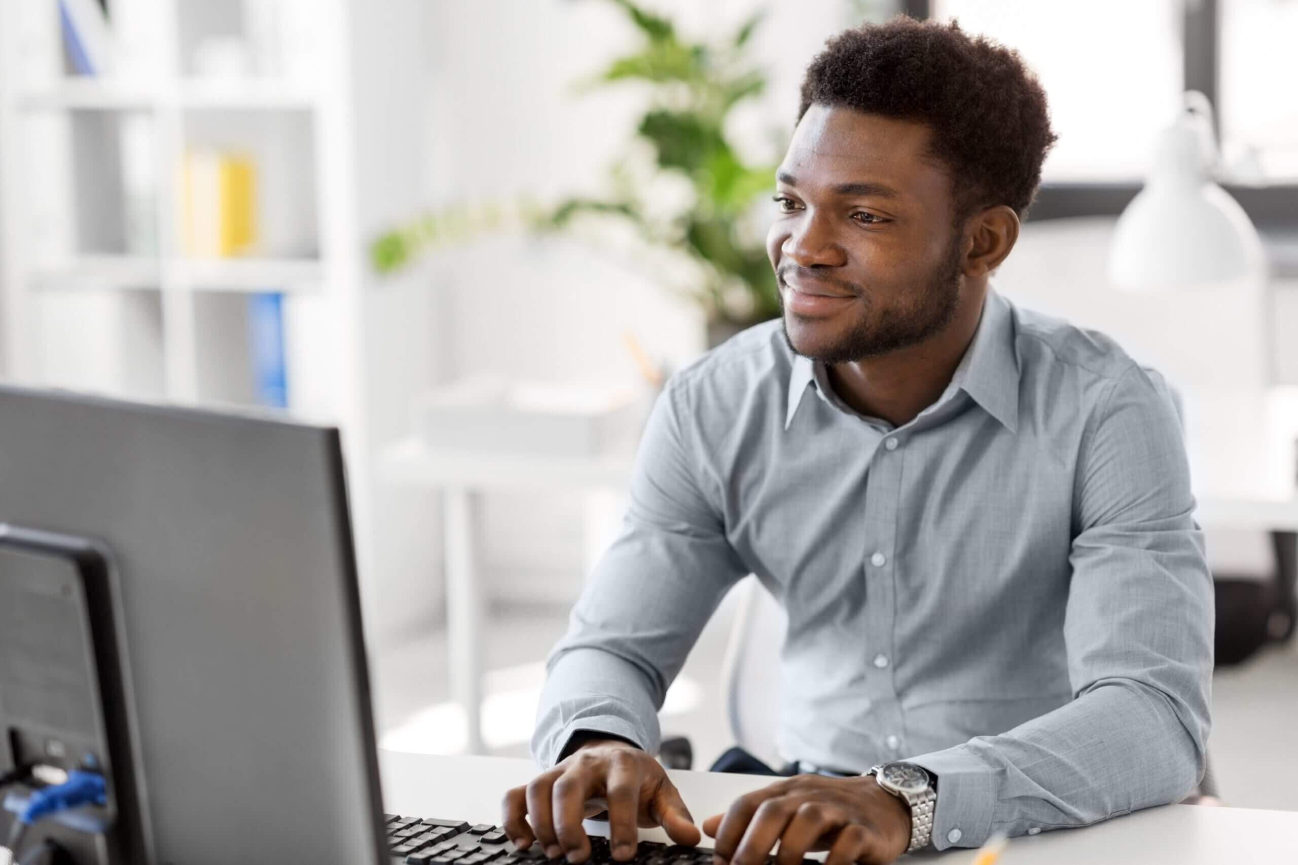Home negro ao computador, sorrindo.