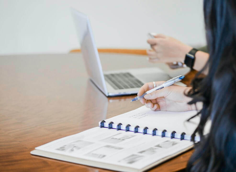 Mulher fazendo anotações em calendário enquanto outra mexe no computador.