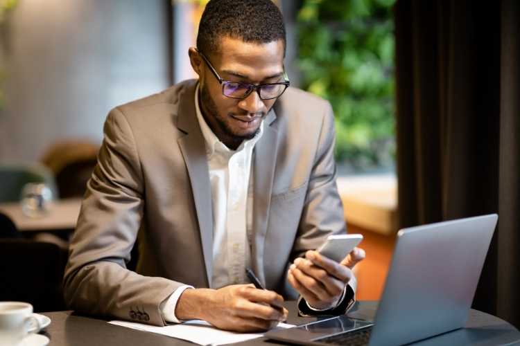 Homem negro de óculos anotando dados de pesquisa em um caderno.