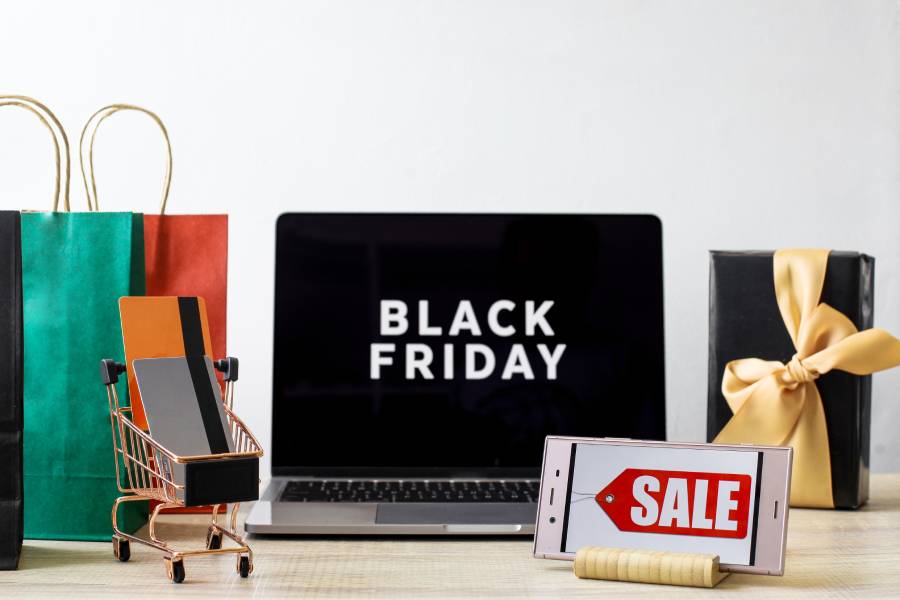 Laptop com 'Black Friday', carrinho miniatura e sacolas, ilustrando o atendimento na Black Friday em marketplaces. 