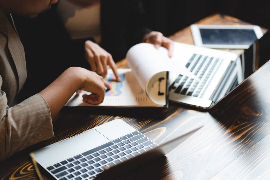 Duas pessoas analisando gráficos em relatório impresso ao lado de laptops, alinhando uma estratégia para vender mais com base em dados