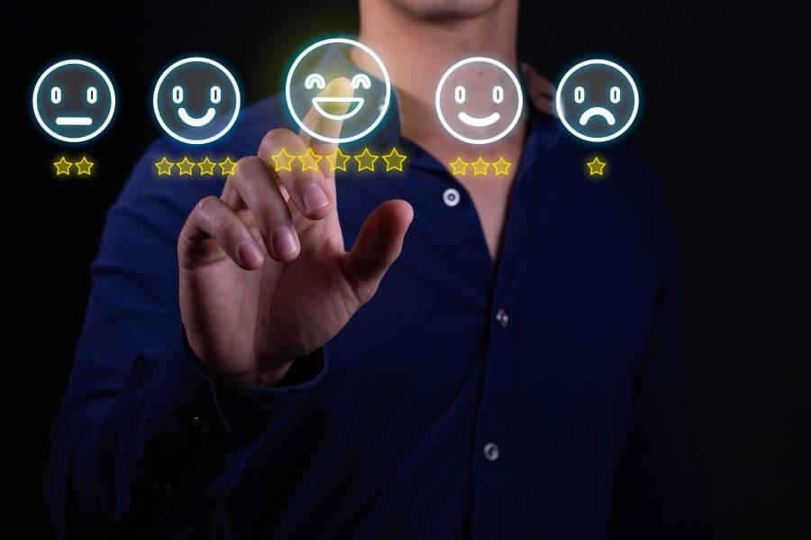 Pessoa apontando o dedo para ícones digitais de emoji com avaliações em estrelas, selecionando a nota máxima em uma pesquisa de satisfação do cliente