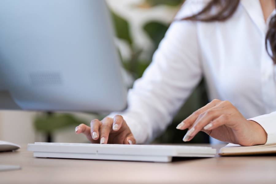 Mãos de mulher digitando em teclado branco de computador em ambiente de escritório, ilustrando o controle de qualidade no atendimento ao cliente.
