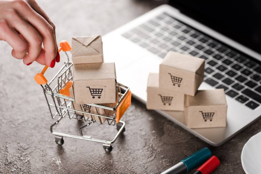Miniatura de carrinho de compras com caixas ao lado de laptop, representando vendas de "Vendedor Indicado" Shopee