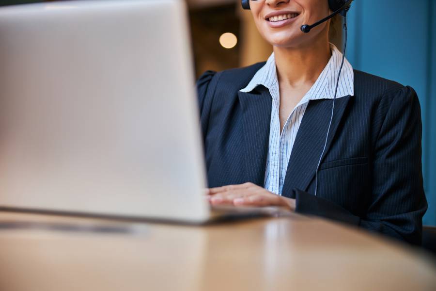 Atendente sorrindo com headset durante atendimento via notebook.